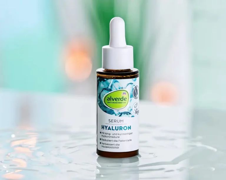 Ein Fläschchen mit Hyaluronserum steht auf einer spiegelnden Fläche. Drumherum ist Hyaluron Serum verteilt. Im Hintergrund sind unscharf Farbflächen in grün, türkis und blau sowie warmtonige Reflexionen zu sehen. Produktfotograf Frankfurt Klaus Ohlenschläger