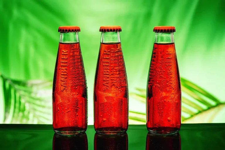 Produktaufnahme mit 3 roten Flaschen Sanbitter vor grünem Hintergrund mit Palmwedeln. Studio für Produktfotografie Klaus Ohlenschlaeger, Frankfurt-Kronberg