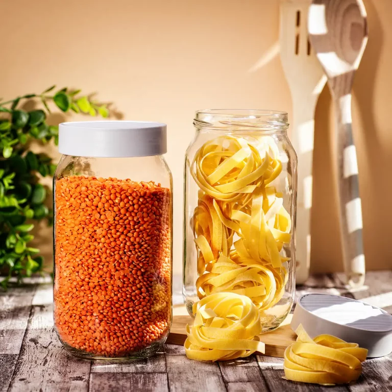 Produktfotografie mit zwei Vorratsgläsern mit roten Linsen und Tagliatelle auf einem Holztisch mit Grünpflanze und Holzbesteck im Hintergrund. Studio für Produktfotografie Klaus Ohlenschlaeger