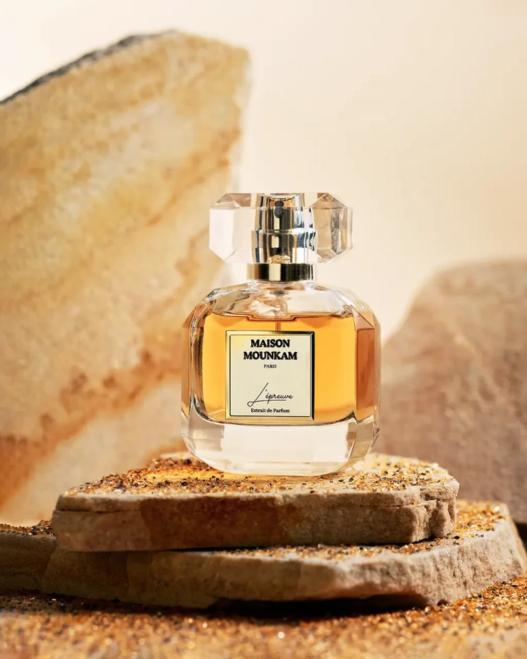 Flakon mit Parfum von MaisonMounkam auf zwei Bruchstücken von Steinplatten aus Sandstein mit zwei weiteren Sandsteinen unscharf im Hintergrund. Produktfotografie Klaus Ohlenschläger, Frankfurt-Kronberg